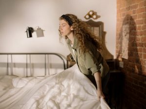 A woman arranging bed linens in a warm, cozy bedroom setting.