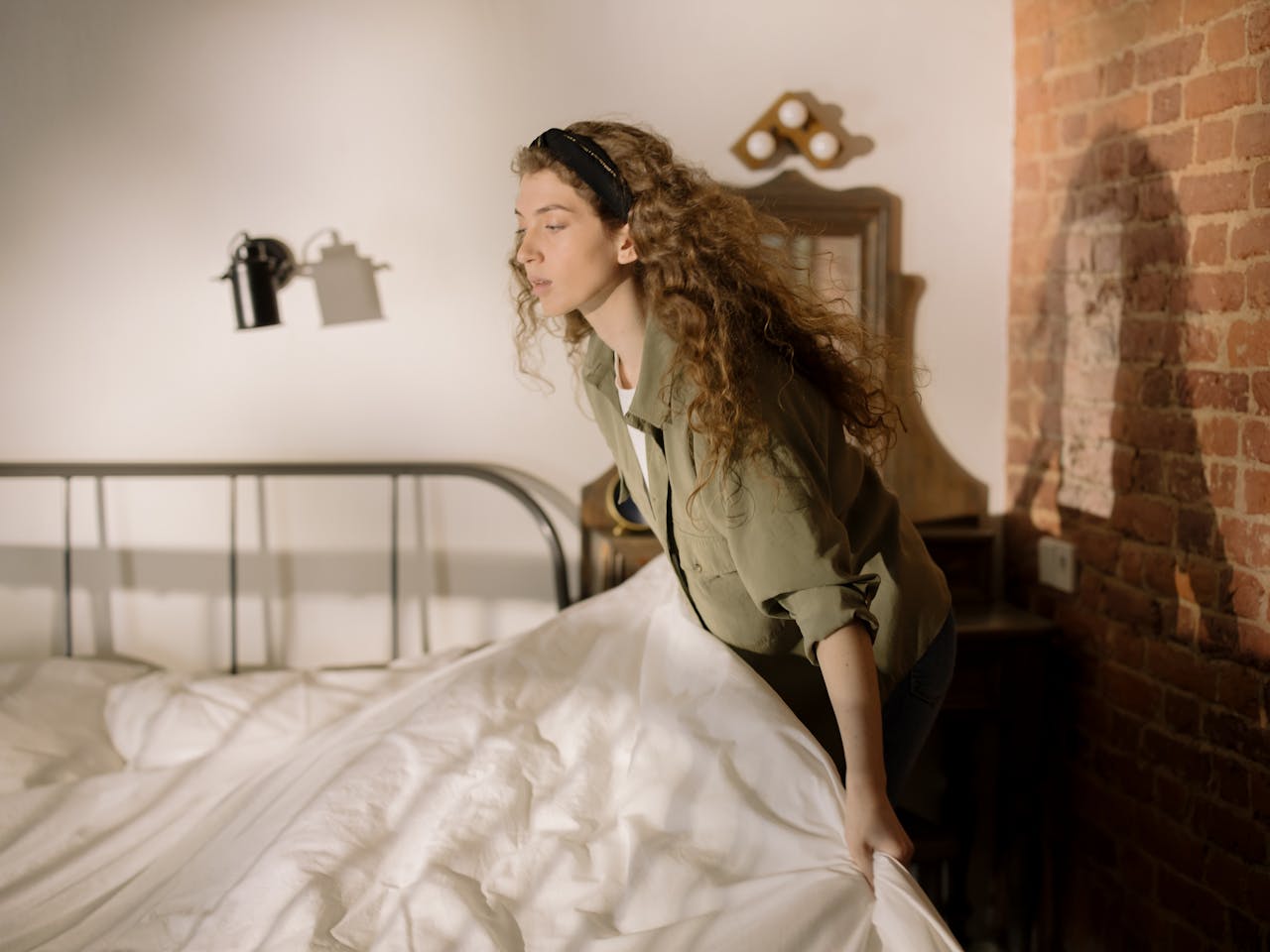 A woman arranging bed linens in a warm, cozy bedroom setting.